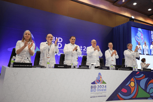 A group of people sitting at a table with their hands raised - Sustainable Development - Inter-American Development Bank - IDB