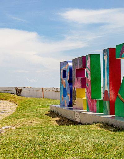 Coastal road beside a lighthouse, with giant colorful painted concrete letters spelling out the name Belize.