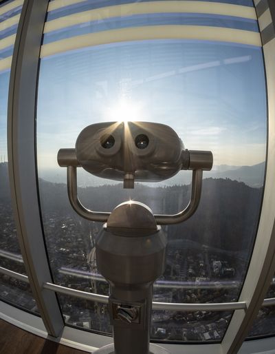 Coin-operated binoculars overlooking a city skyline through a curved glass window.