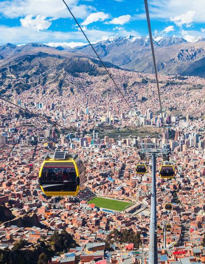 Panoramic view of La Paz, Bolivia, with a cable car crossing above the densely built city and mountains in the background.