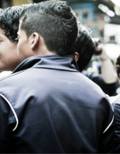 Young people holding cameras in a crowded outdoor setting, with one woman looking to the side while holding a DSLR camera.