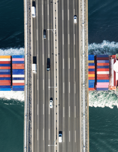 A cargo ship passing under a highway bridge.