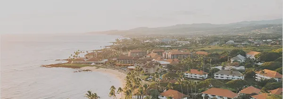 Aerial view of a tropical coastal resort with red-roofed buildings, a sandy beach, and palm trees at sunset