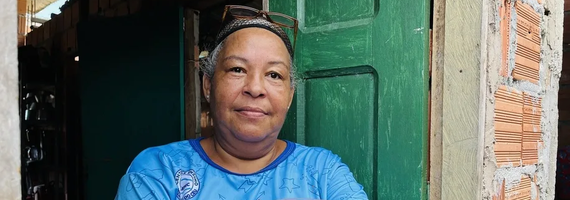 A middle-aged woman with grey hair and glasses on her head, smiling in front of a green door and an unfinished brick wall