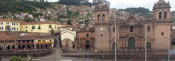The ornate stone facade of the Cusco Cathedral in Peru, with colonial buildings and a hillside neighborhood in the background