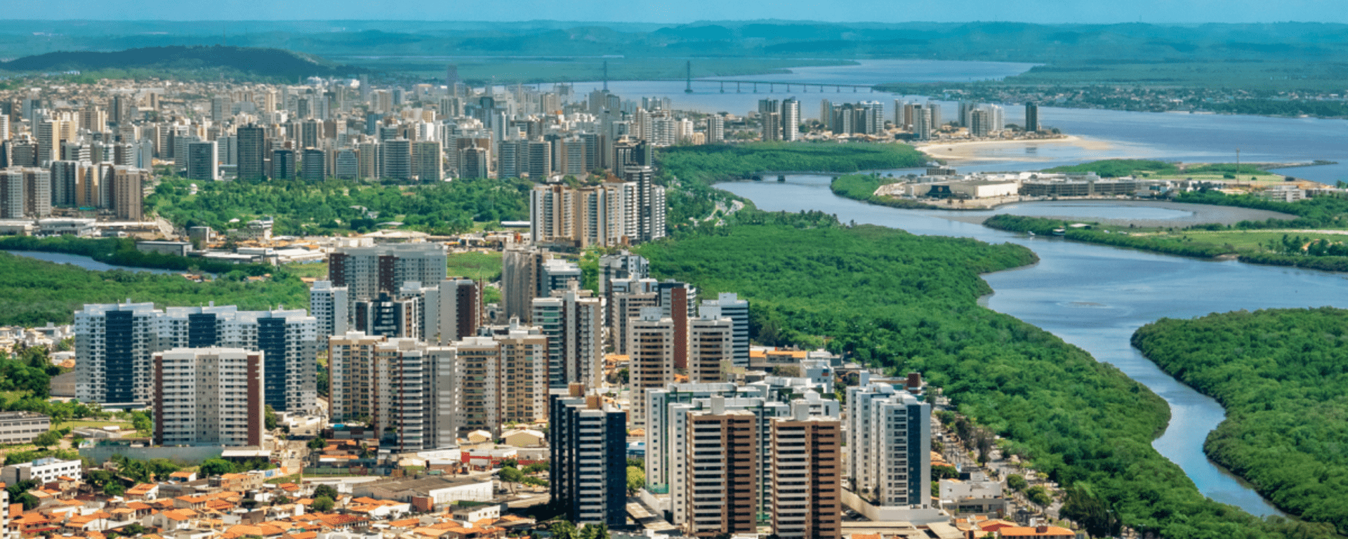 Panoramic day view of a city with trees and buildings and a river alongside - Inter American Development Bank - IDB Invest