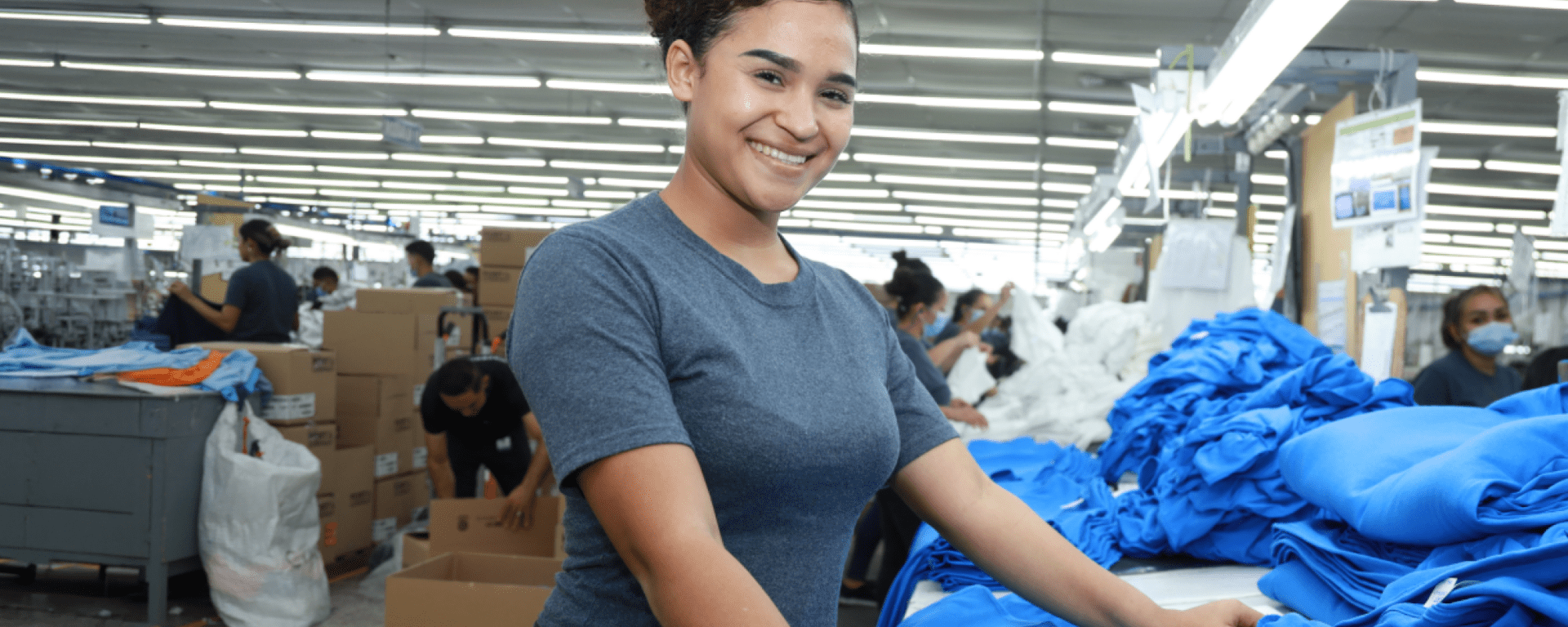 Woman smiling with a clothing factory in the background - Inter American Development Bank - Impact Evaluation