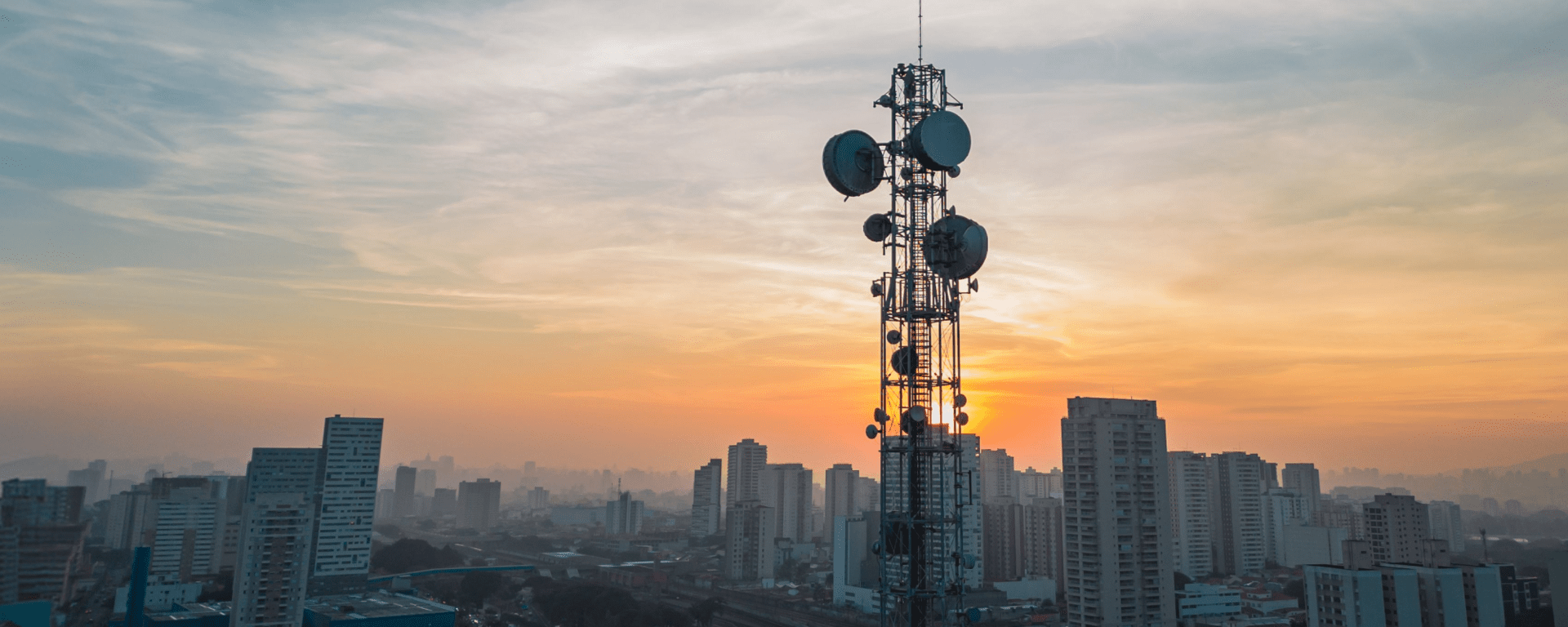 Telecommunications tower rising above an urban skyline at sunset, IDB.