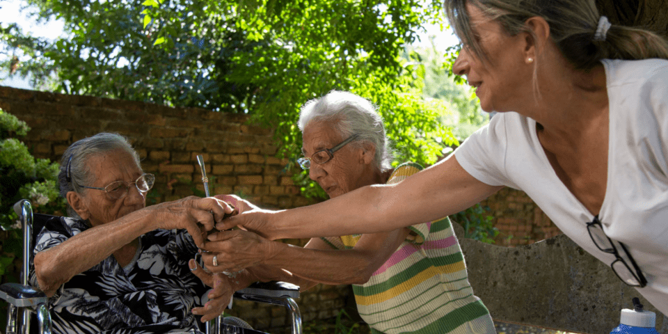Woman in a wheelchair and adult women holding hands - Inter American Development Bank - Long-Term Care