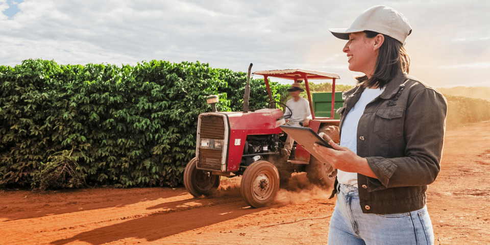 Woman holding her hands in front and a tractor in the background in front of a farm crop - Inter American Development Bank - Fiscal Management