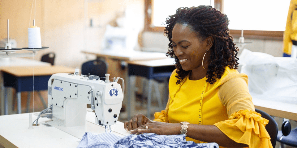 Afro-descendant woman smiling while sitting in front of a sewing machine - Inter American Development Bank - Climate Resilience