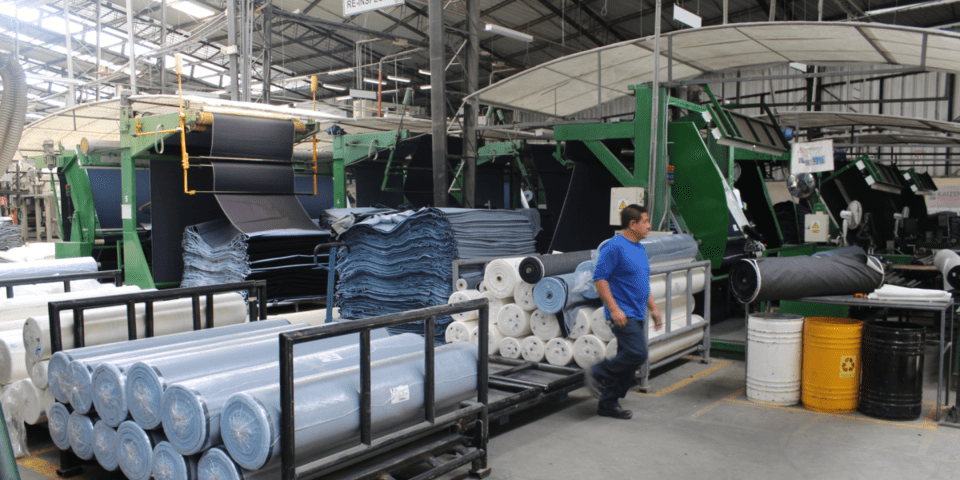 Worker walking among large rolls of plastic inside a factory - Inter American Development Bank - IDB Invest