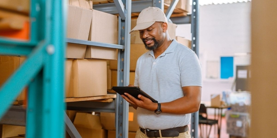 Smiling worker in a factory surrounded by boxes - Inter American Development Bank - IDB Invest