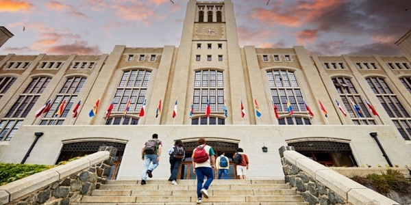 Grupo de alumnos subiendo las escalinatas de una institución de enseñanza monumental, vistos desde abajo y de espaldas