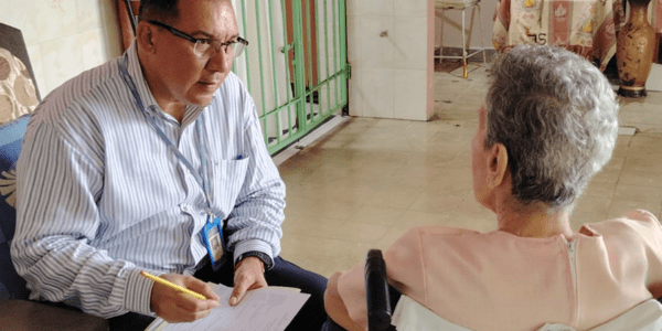 Hombre mayor encuestando a una mujer mayor usuaria de silla de ruedas.