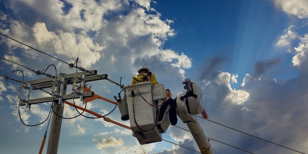 Utility worker in a bucket lift repairing overhead power lines under a partly cloudy sky.