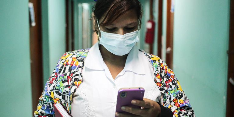 A woman wearing a mask and holding a phone. Health - Inter-American Development Bank - IDB