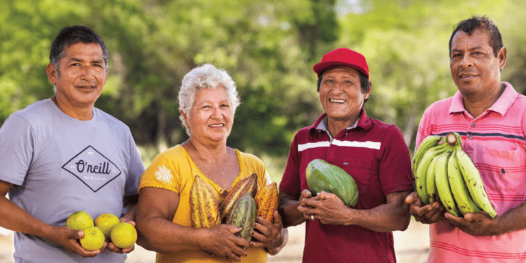 Adults holding fruit in their hands and a forest in the background - Inter American Development Bank - IDB Corporate
