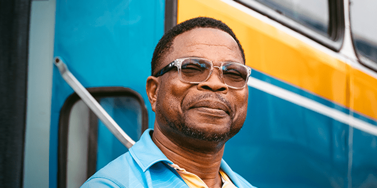 Afro-descendant man smiling and a bus behind him - Inter American Development Bank - Impact Framework