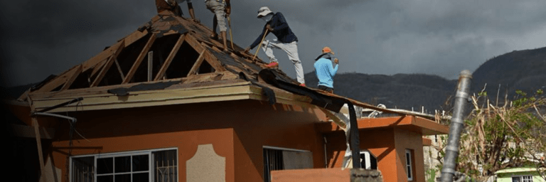 Men on the wooden roof of a house under construction - Inter American Development Bank - Disaster Management