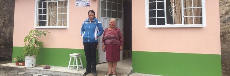 Two women smiling in front of a house - Inter American Development Bank - IDB