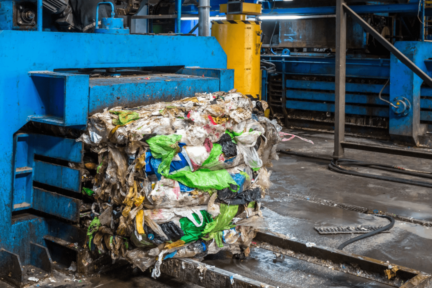Máquina industrial azul compactando una gran pila de residuos sólidos mixtos en una instalación de reciclaje