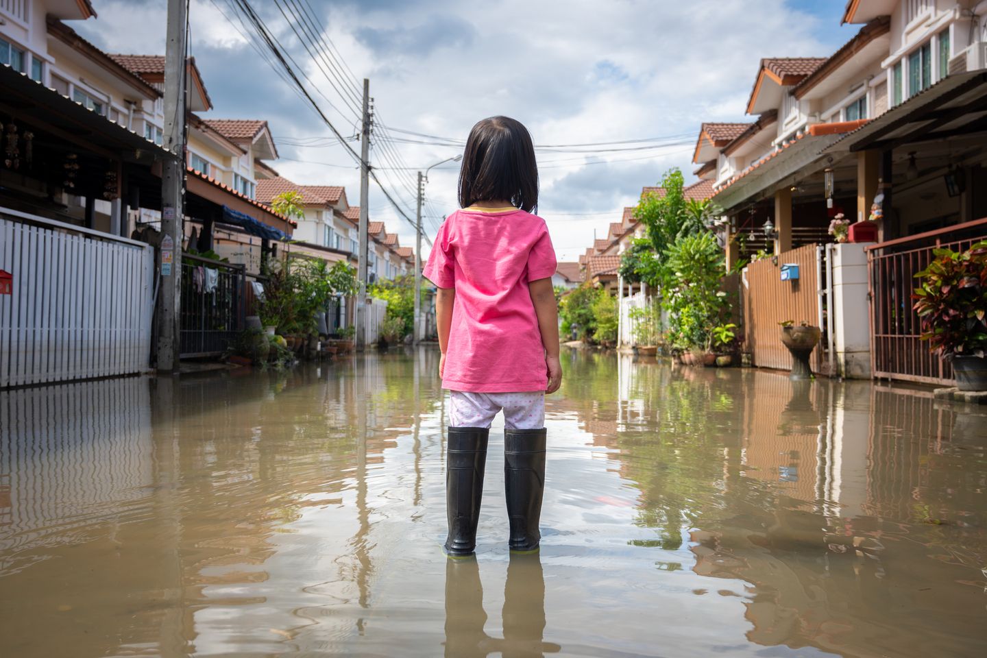 Uma menina parada no meio de uma rua alagada, com casas aos lados