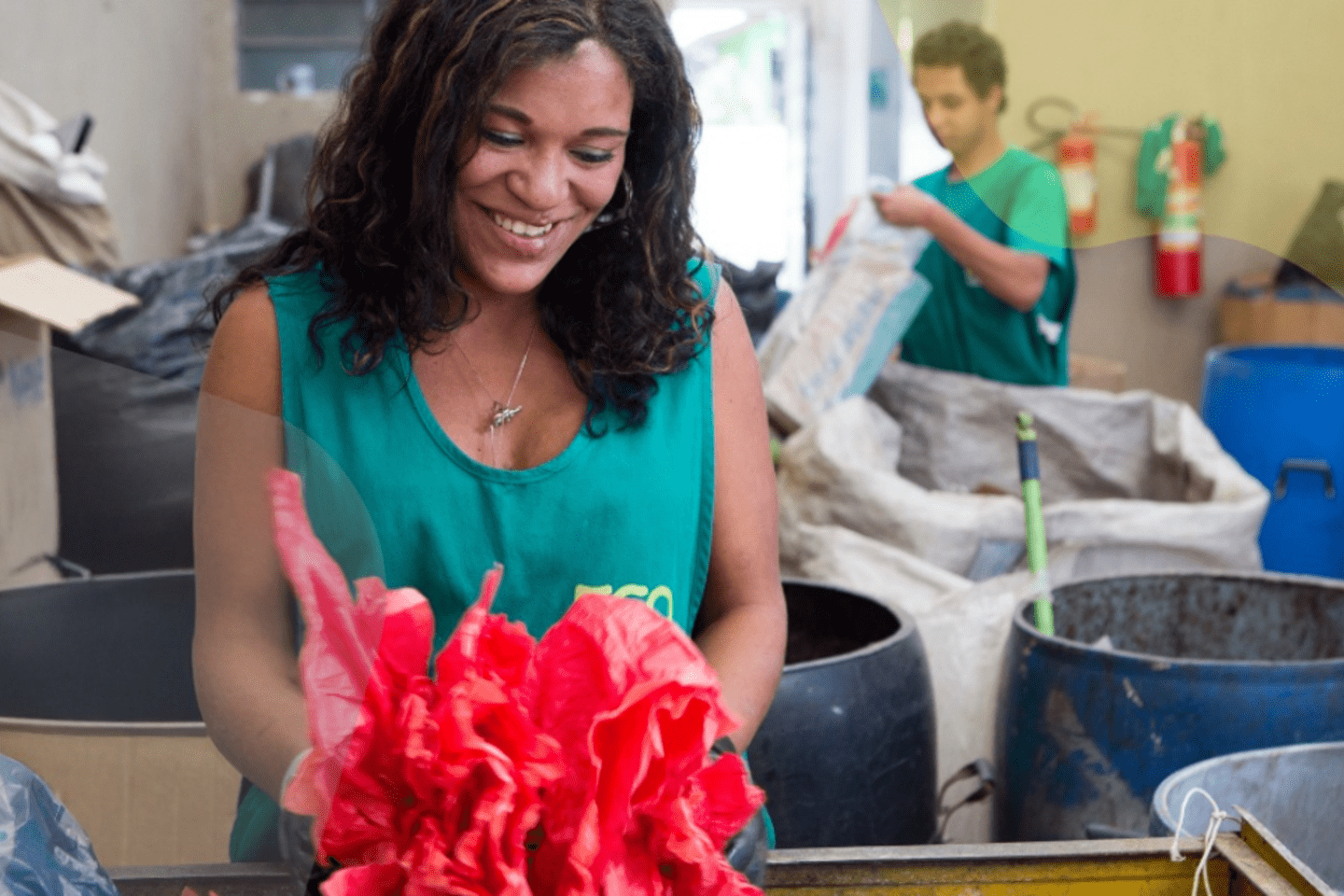 Mujer sonriente sostiene materiales reciclables en una instalación de economía circular junto a un compañero de trabajo.
