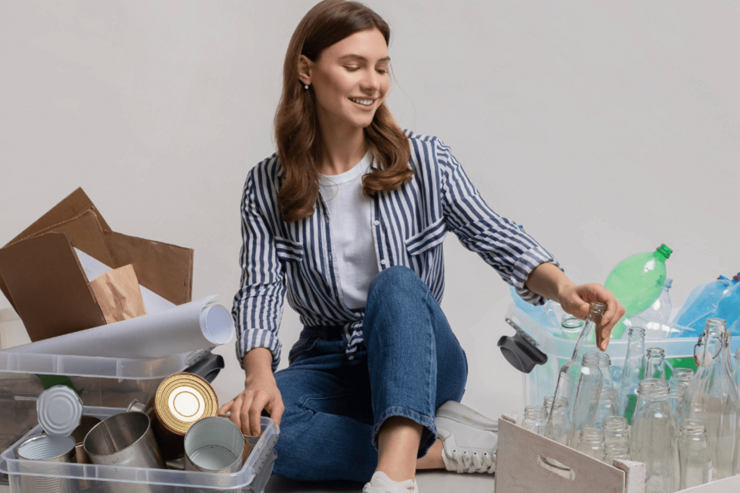 Portrait of young woman sitting among containers with solid waste and raw recycle material. 