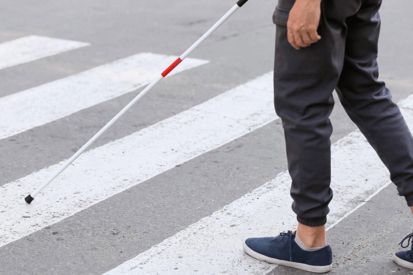persona cruzando una calle por un paso de peatones, utilizando un baston blanco para orientarse