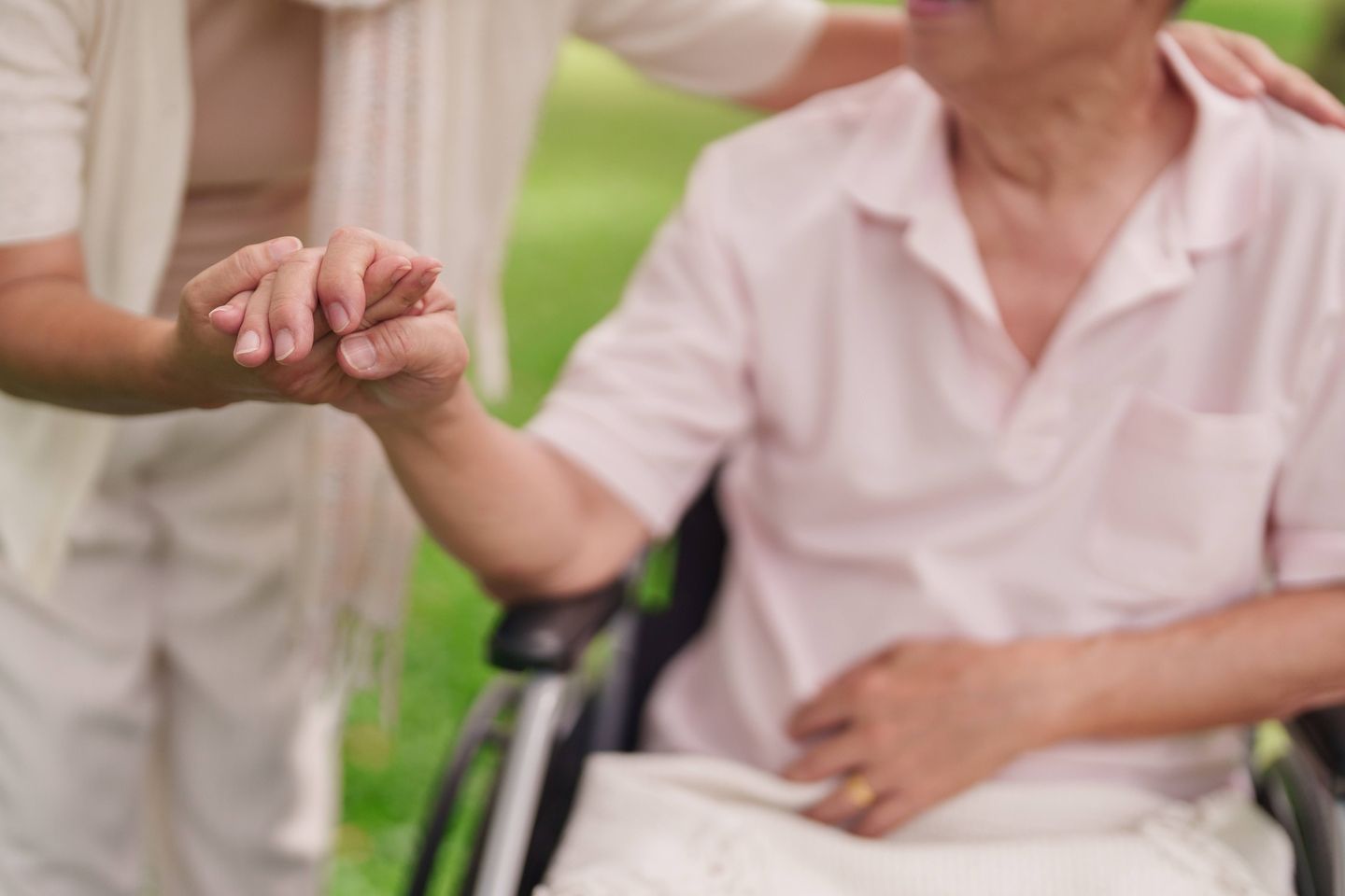 a caregiver holding the hand of an older person who is a wheelchair
