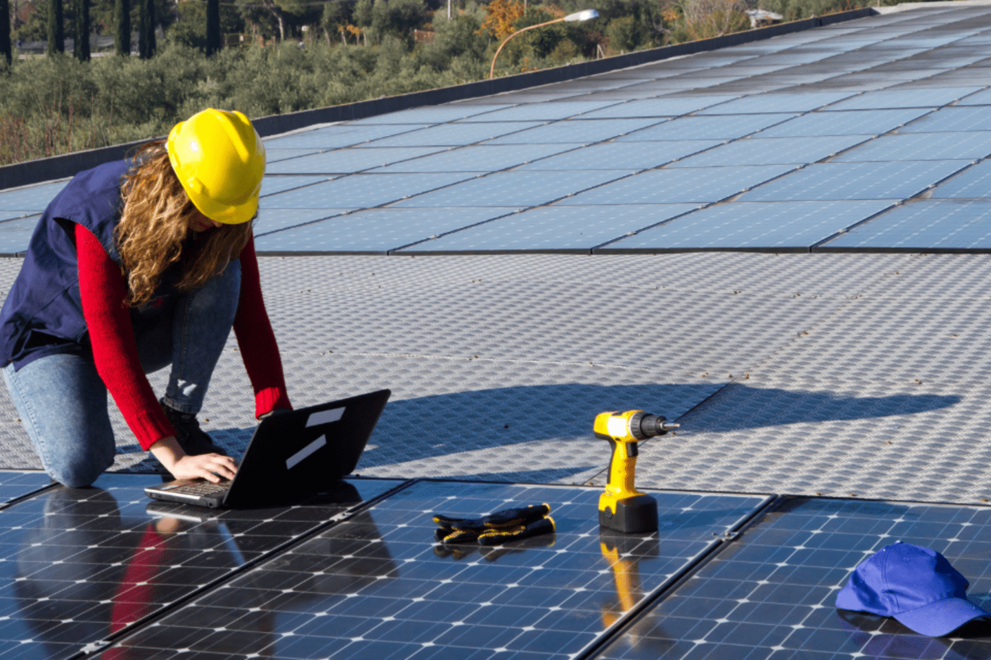 Mujer ingeniera con sombrero de obra amarillo agachada trabajando en una laptop sobre panales solares 