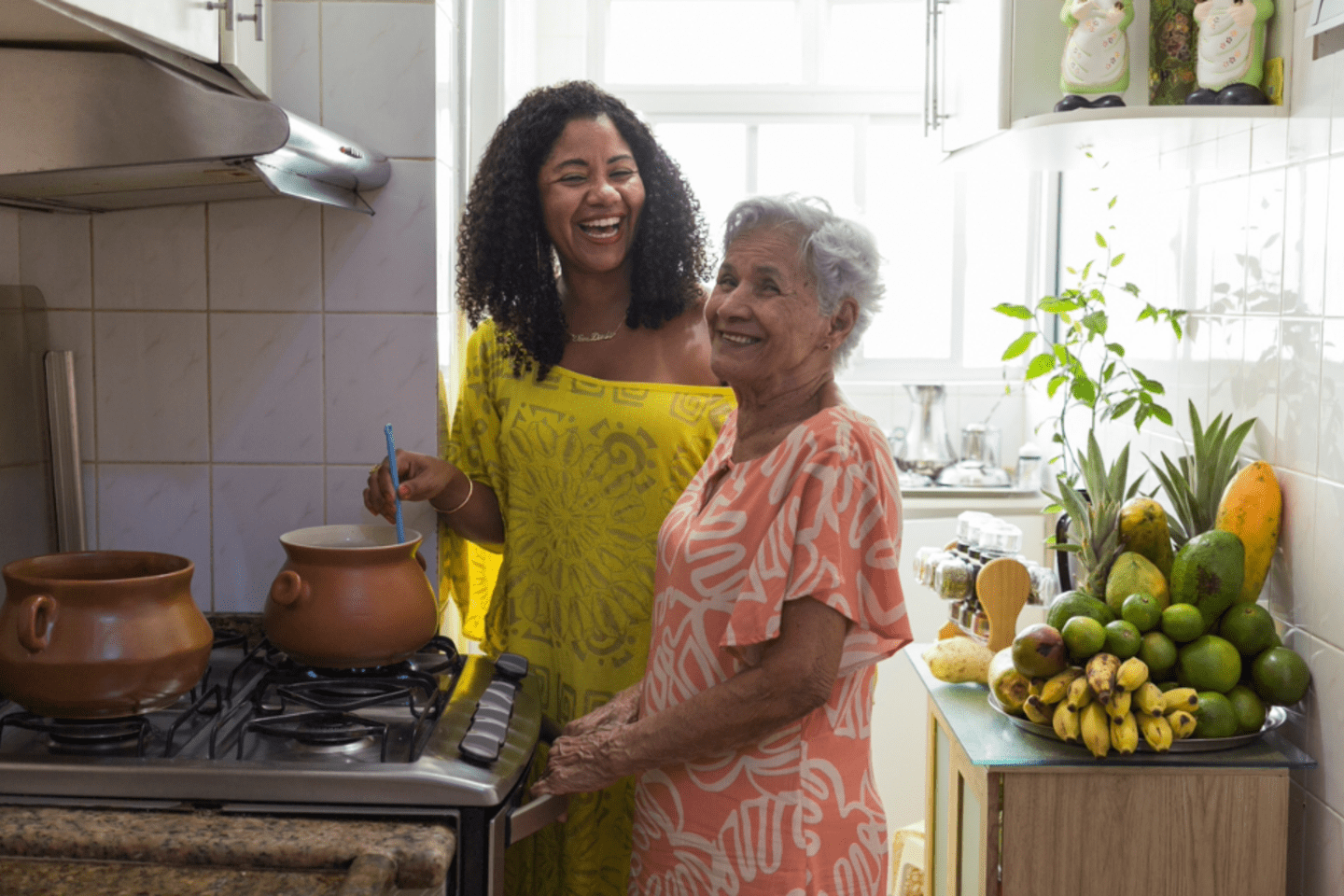 Mujer joven sonriendo mientras cocina con su madre mayor también sonriendo