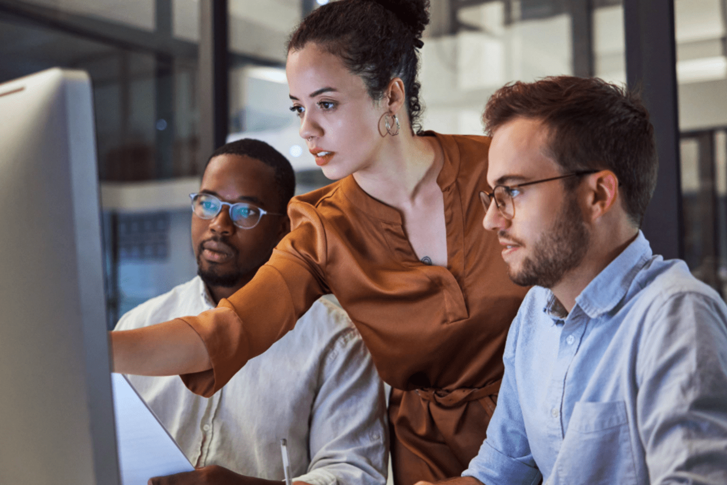 Una mujer afrodescendiente, un hombre afrodescendiente y un hombre blanco trabajando juntos en una computadora usando IA