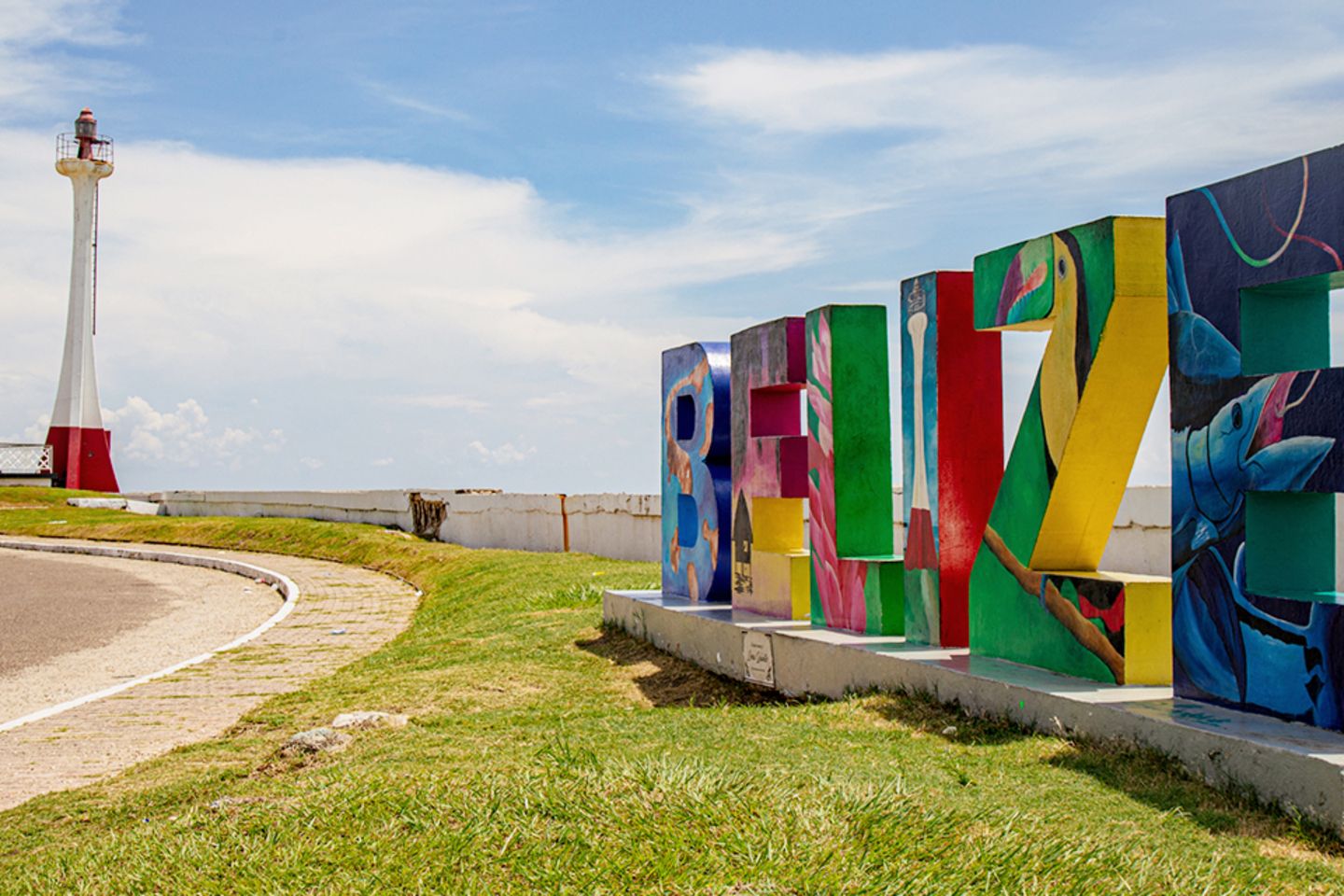 Coastal road beside a lighthouse, with giant colorful painted concrete letters spelling out the name Belize.