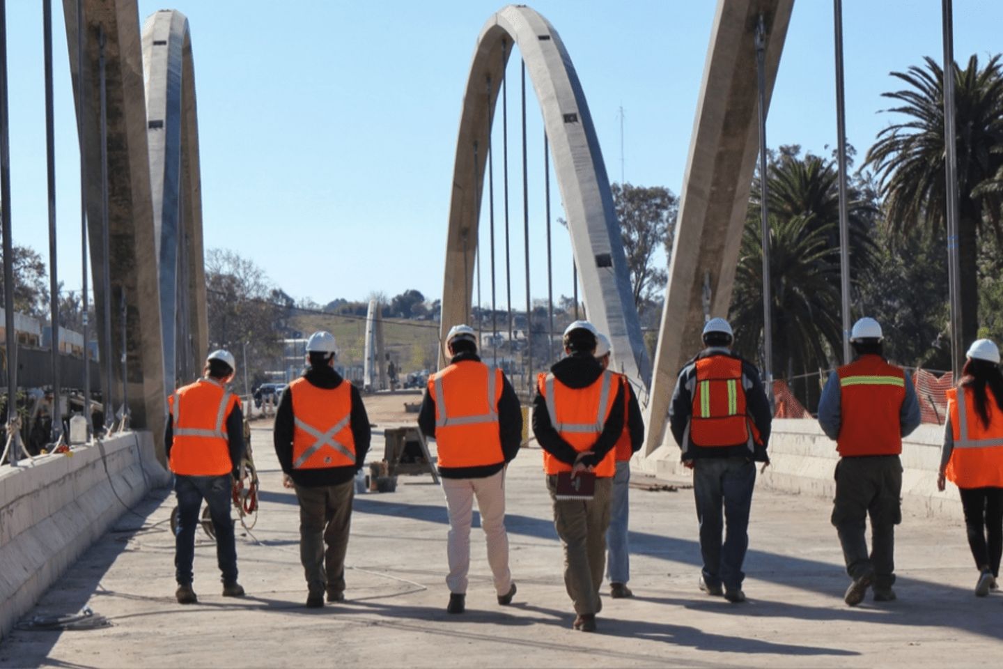 Construction workers in safety vests and hard hats walking across a bridge.