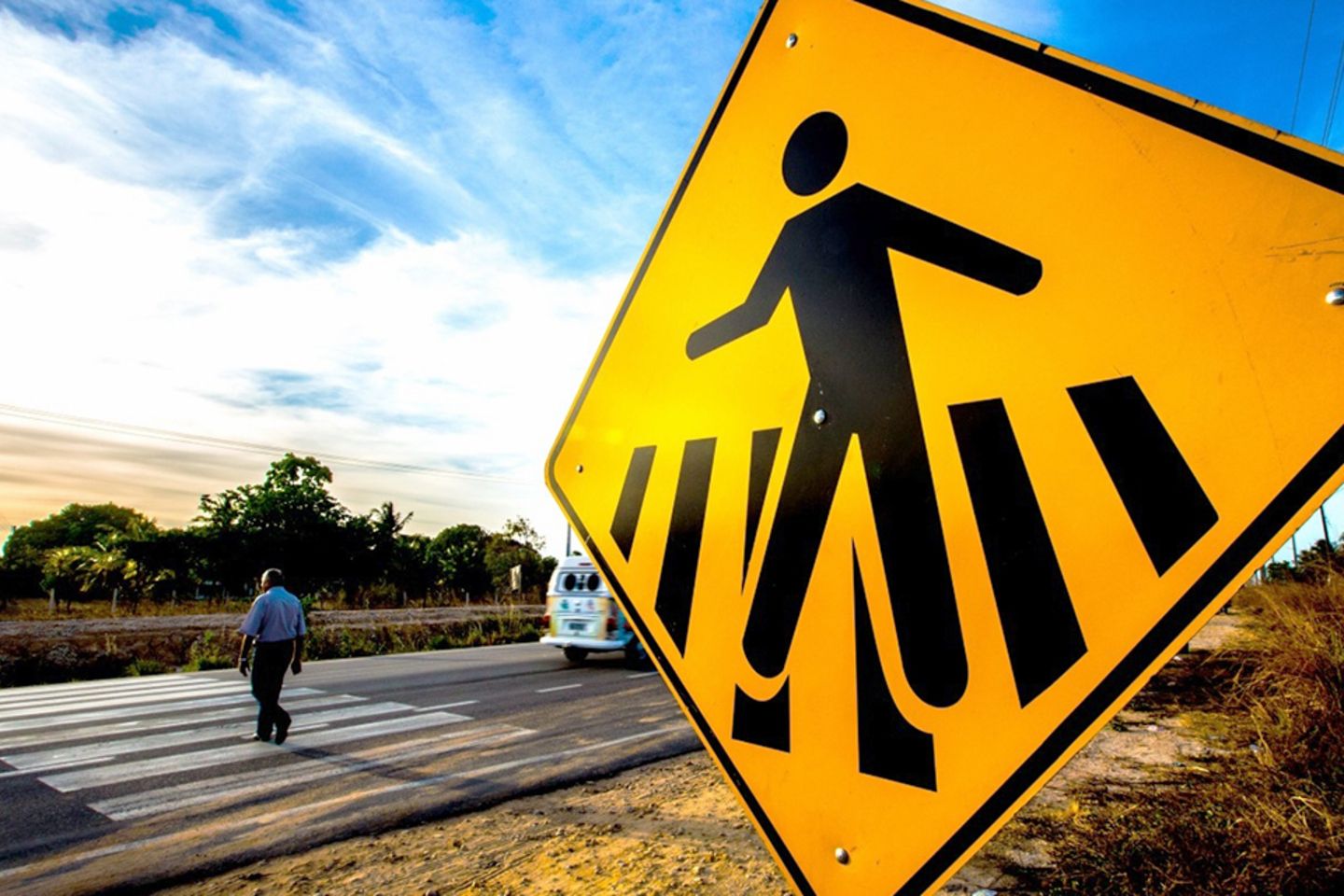 Close-up of a pedestrian crossing sign, with a man crossing the street in the background.
