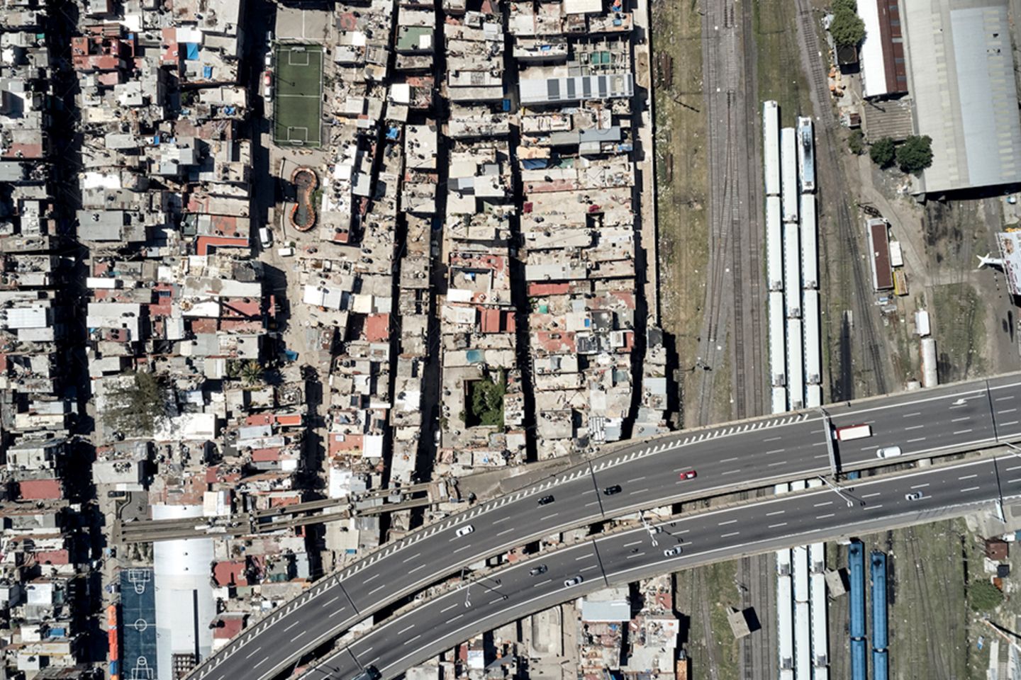 Aerial view of a dense urban neighborhood beside railway tracks and an elevated highway.