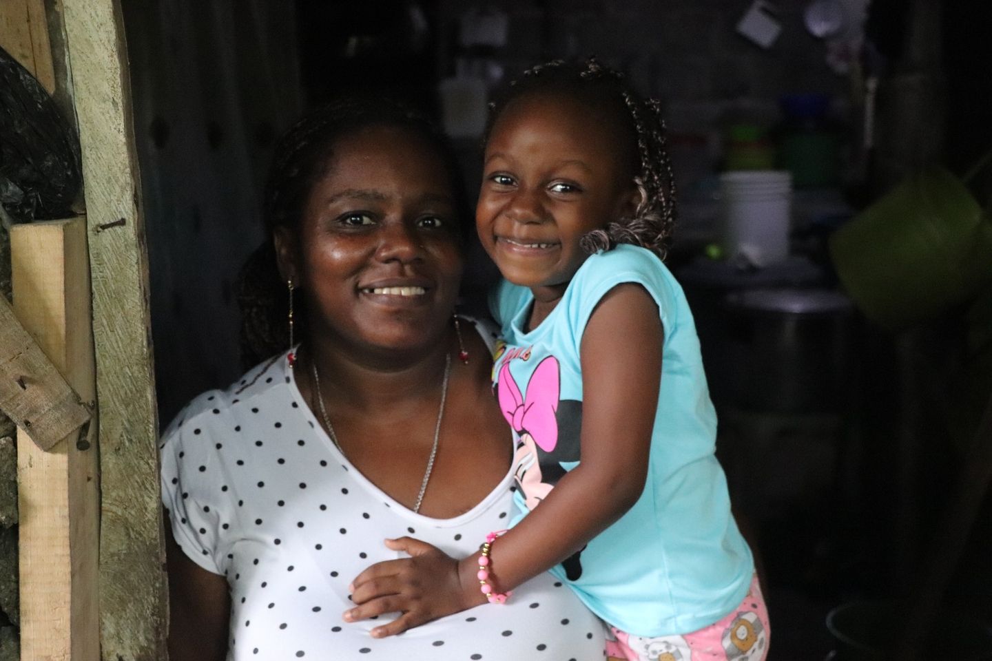 Mujer mirando a la cámara sonriendo con una niña en brazos. 