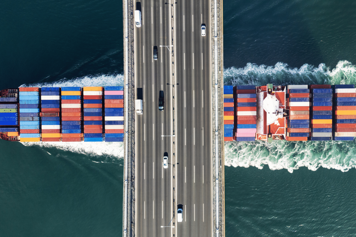 A cargo ship passing under a highway bridge.