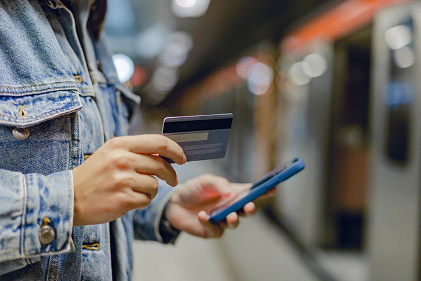 Woman's hand holding mobile phone and credit card at subway station