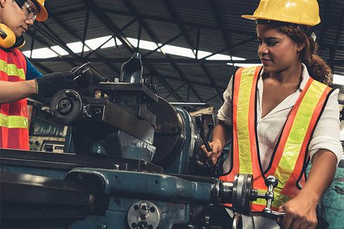 A woman wearing a hard hat and safety vest working on a machine. Jobs and Development - Inter-American Development Bank - IDB