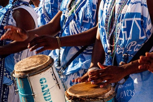 Group of people wearing blue and white outfits playing drums. Gender Equity - Inter-American Development Bank - IDB