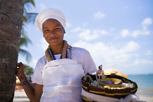 Woman wearing a white dress and a white head wrap holding a bag. Economic Development - Inter-American Development Bank - IDB
