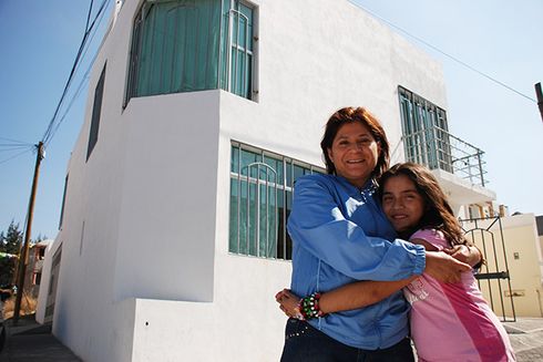 A woman and a child hugging in front of a white building. Transport - Inter-American Development Bank - IDB