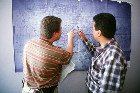 A couple of men looking at a map in the wall. Economic Development - Inter-American Development Bank - IDB