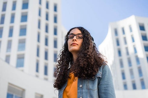 Person with long curly hair wearing glasses and a denim jacket. Inclusion - Inter-American Development Bank - IDB
