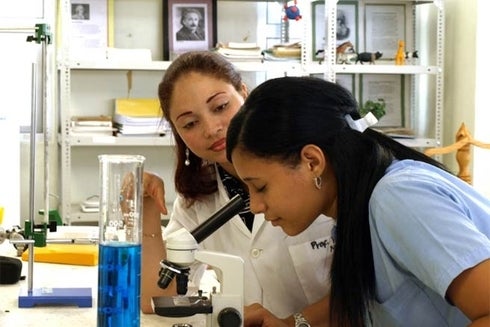A woman in a laboratory looking through a microscope. Education - Inter-American Development Bank - IDB