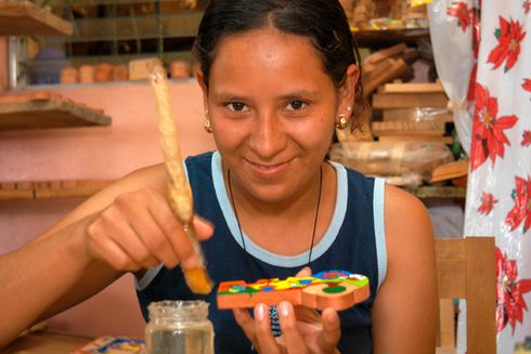 A girl is smiling while painting a wood block - Inter-American Development Bank - IDB