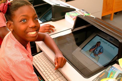 A girl smiles sitting in front of a computer - Inter-American Development Bank - IDB